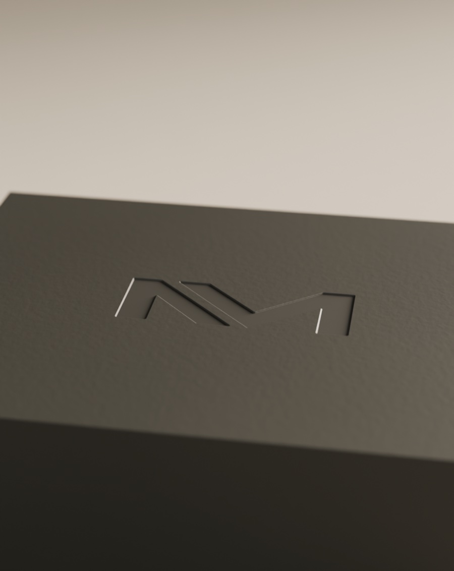 Monograma Nivenmark hundido en bajorrelieve sobre la tapa de un estuche de polímero mate carbón, revelado por una luz rasante.